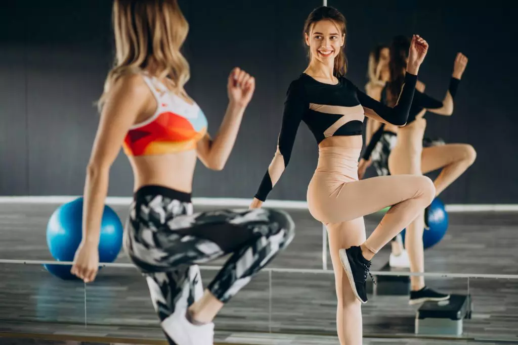 Alunos engajados com a aula de step na academia, na imagem mostra mulheres dando sorriso enquanto fazem os exercícios em pé