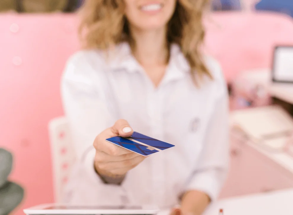 Recepcionista de academia entregando cartão de crédito para aluno após pagamento em crédito recorrente
